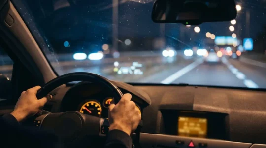 Volant moderne avec mains du conducteur et affichage tête haute ADAS sur pare-brise pendant conduite nocturne autoroutière